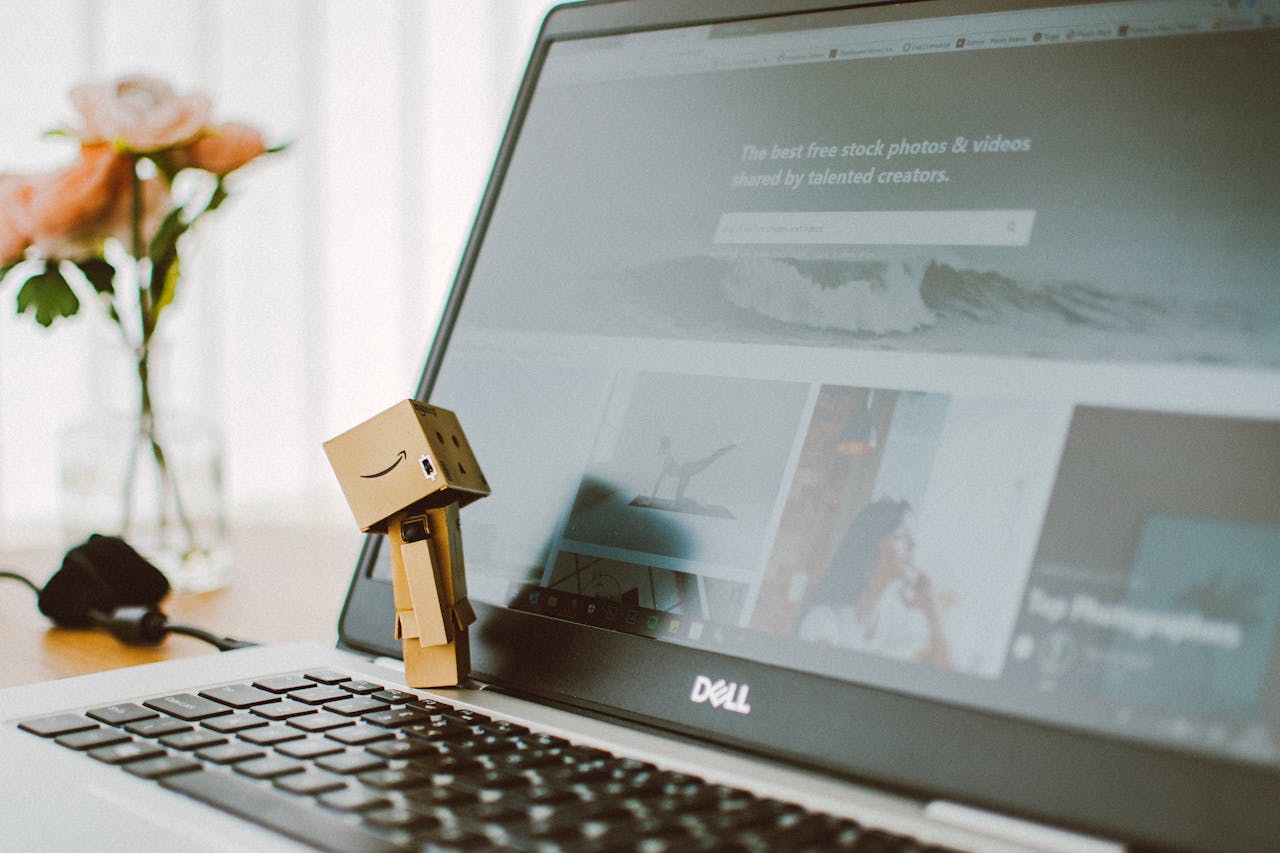 A small toy figure stands on a laptop keyboard with flowers in the background.